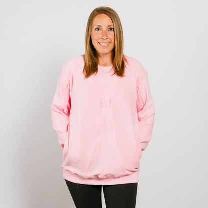 Woman wearing a pink crewneck sweatshirt with long sleeves and black pants, smiling at camera.