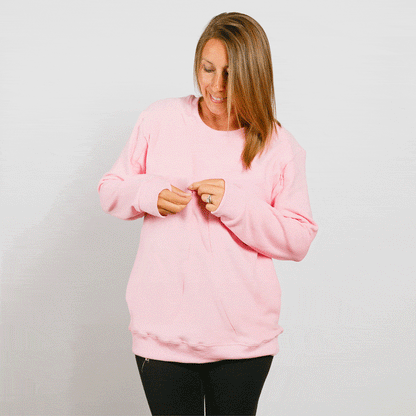 Woman wearing a pink crewneck sweatshirt and black pants, looking down while adjusting the neckline.