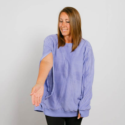 Woman wearing a light purple crewneck sweatshirt with extended sleeves over black pants.