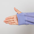 Child's hand extended from light purple long-sleeved shirt with ribbed cuff against gray background.