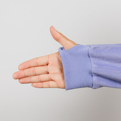 Child's hand extended from light purple long-sleeved shirt with ribbed cuff against gray background.