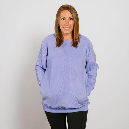 Woman wearing a light purple crewneck sweatshirt with hands in pockets and black pants.