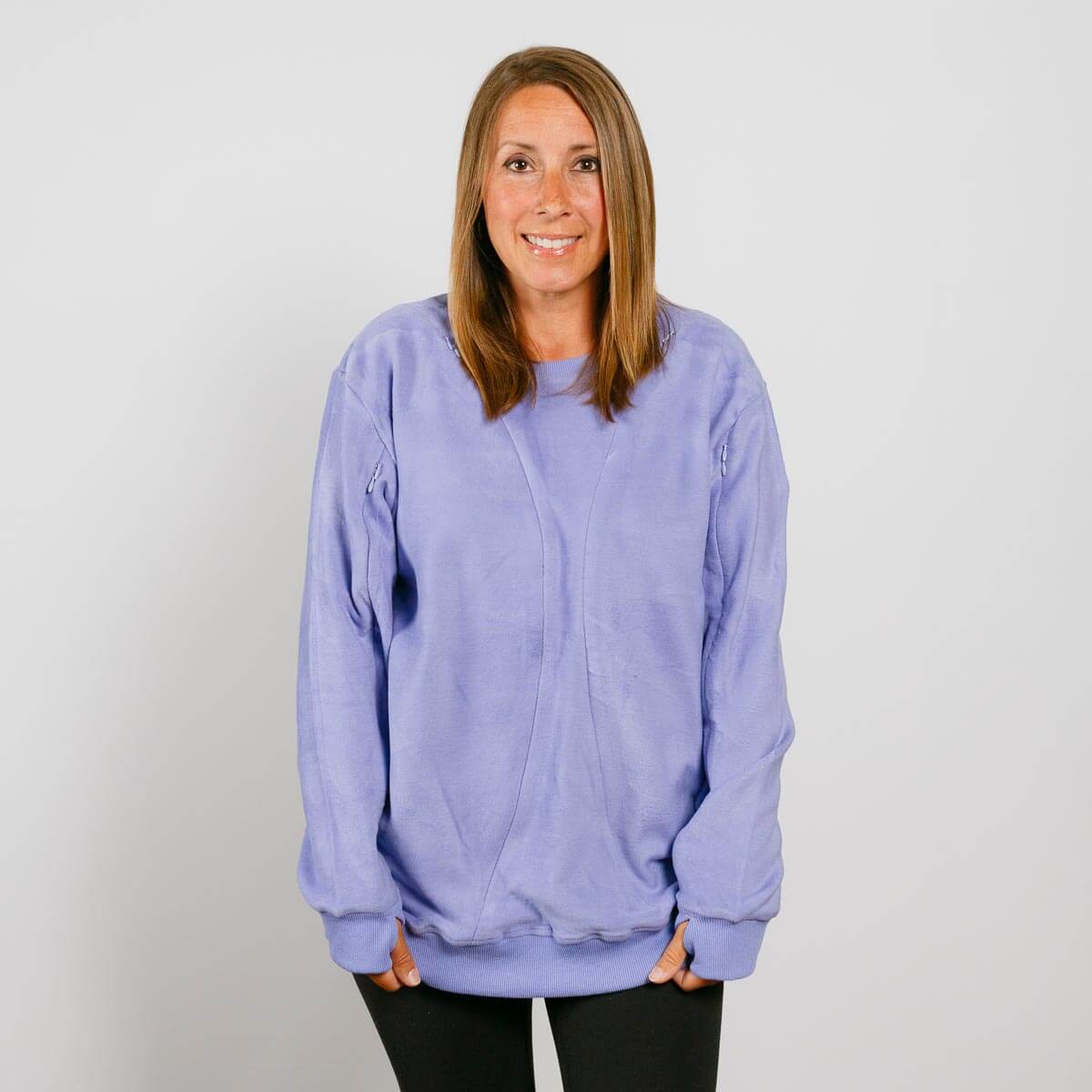 Woman wearing a light purple crewneck sweatshirt over black pants, smiling at the camera.