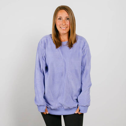 Woman wearing a light purple crewneck sweatshirt over black pants, smiling at the camera.