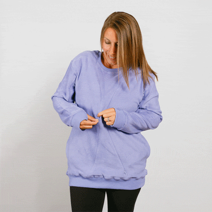 Woman wearing a light purple crewneck sweatshirt over black pants, looking down while adjusting the garment.