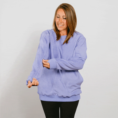 Woman wearing light purple crewneck sweatshirt and black pants, looking downward with hands at chest.