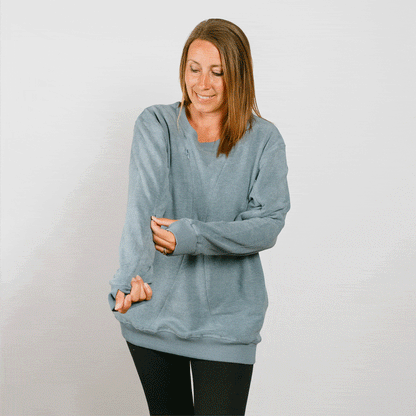 Woman wearing a light blue crewneck sweatshirt over black pants, looking downward.