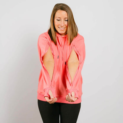 Woman wearing pink hoodie with open side panels and black leggings, smiling at camera.