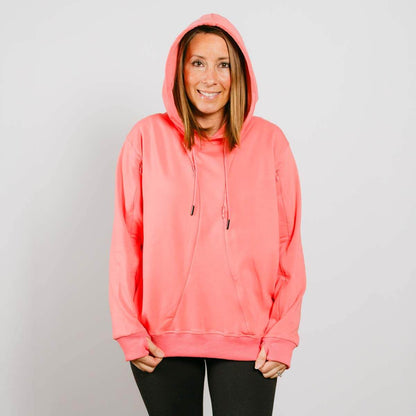 Woman wearing a bright coral pink hoodie with drawstrings and black pants against a white background.