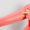 Hand opening a pink zippered sleeve pocket on a coral hoodie against a white background.