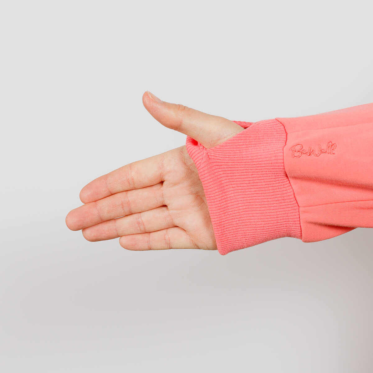 Child's hand extending from coral pink hoodie sleeve with ribbed cuff against neutral background.