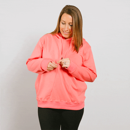 Woman wearing a bright pink hoodie over black pants, looking down while adjusting the front zipper.