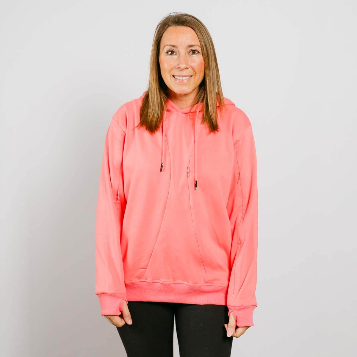 Woman wearing a bright pink hoodie with drawstrings and black pants against a white background.