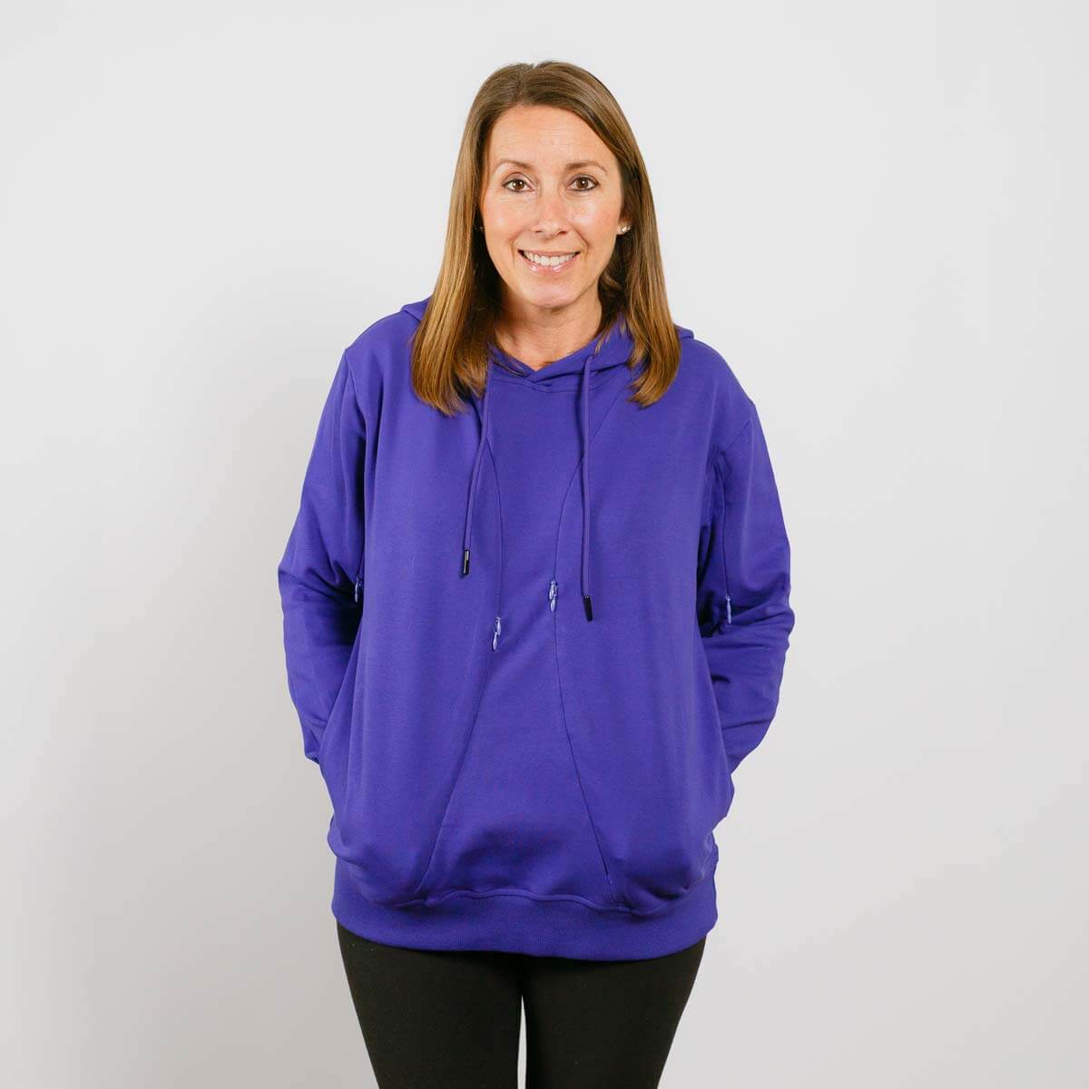 Woman wearing a purple hoodie with drawstrings and front pockets over black pants.