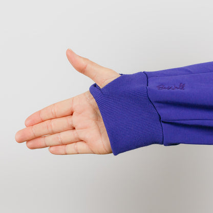 Person's hand and arm wearing a blue hoodie with ribbed cuff against a light gray background.