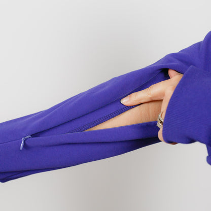 Hand pulling back blue fabric sleeve to reveal hidden thumb hole opening.