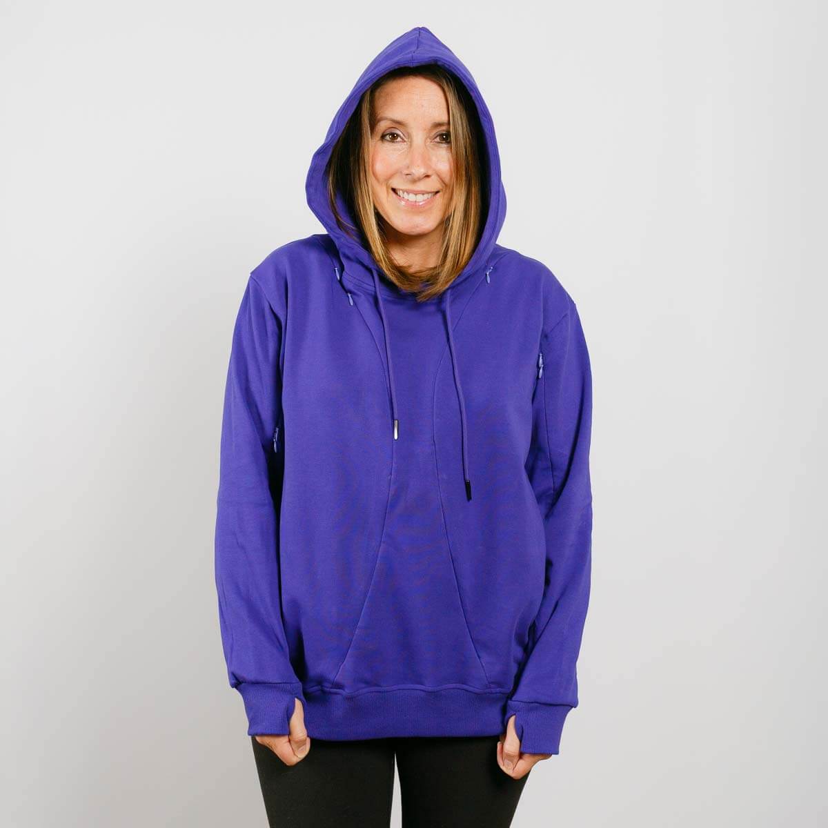 Woman wearing a purple hoodie with drawstrings and black pants against a white background.