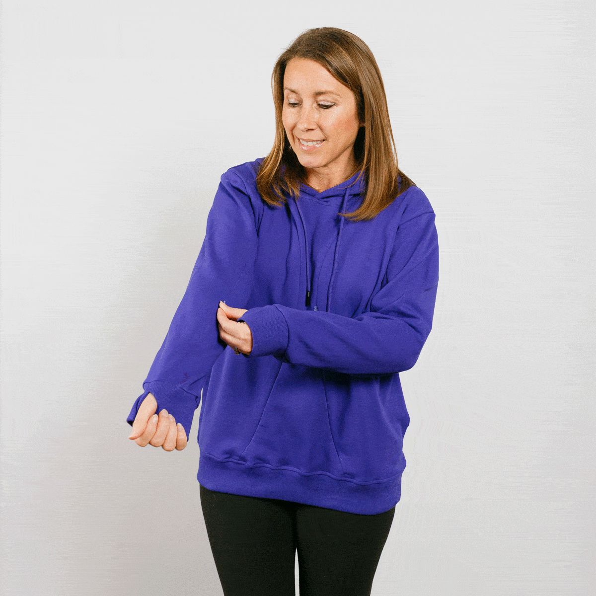 Woman wearing a purple hoodie with black pants, looking down at her arm.