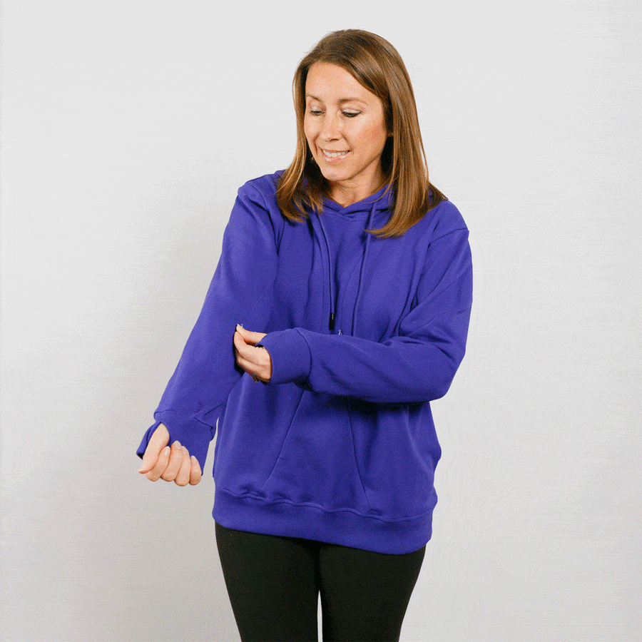Woman wearing a purple hoodie with black pants, looking down at her arm.