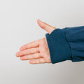 Child's hand extending from navy blue ribbed cuff of zip hoodie against gray background.