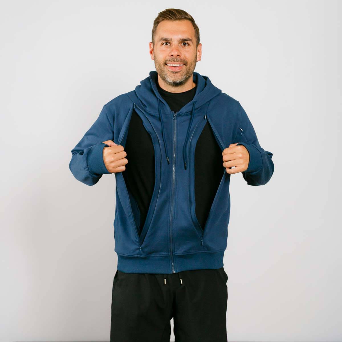 Man wearing a dark  blue hoodie opening both sides of the front via zip up holes with a plain background | Model is 5'8" 165lbs wearing size M