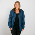 Woman wearing a blue zip-up hoodie over a black shirt against a white background.