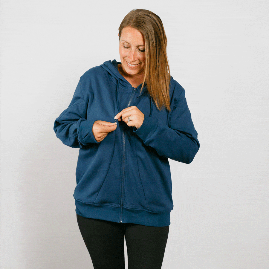 Woman wearing a navy blue zip-up hoodie and black pants, zipping the front closure.