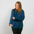 Woman wearing a navy blue zip hoodie with black pants, smiling while looking down.