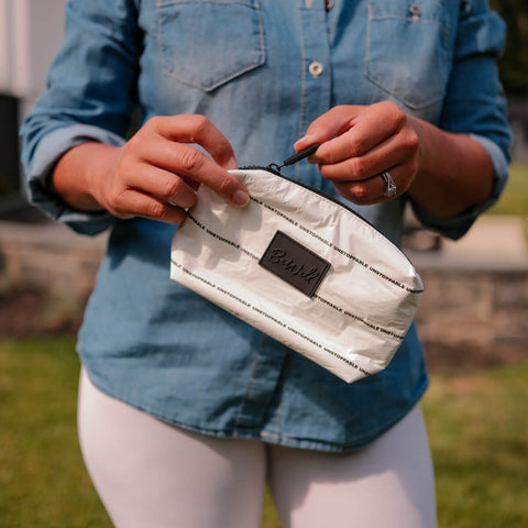 Person in denim shirt holding open a small striped white pouch with a dark label.