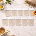 Ten clear mini pill pouches with white zippered tops arranged on marble surface.