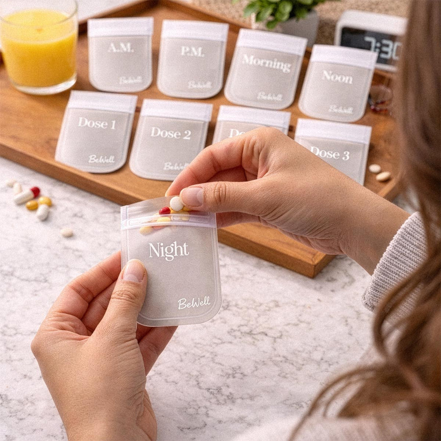 Woman's hands holding clear mini pill pouch labeled "Night" from organizer set displayed on wooden tray.