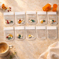 Flat lay of ten clear pill organizer pouches labeled Monday through Sunday with colorful medications inside.