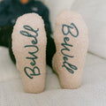 Close-up of beige rest day socks with "BeWell" and "Therapy" text printed on soles.