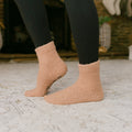 Person wearing tan Rest Day socks with black leggings standing on textured floor.