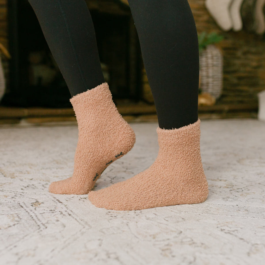 Person wearing tan Rest Day socks with black leggings standing on textured floor.