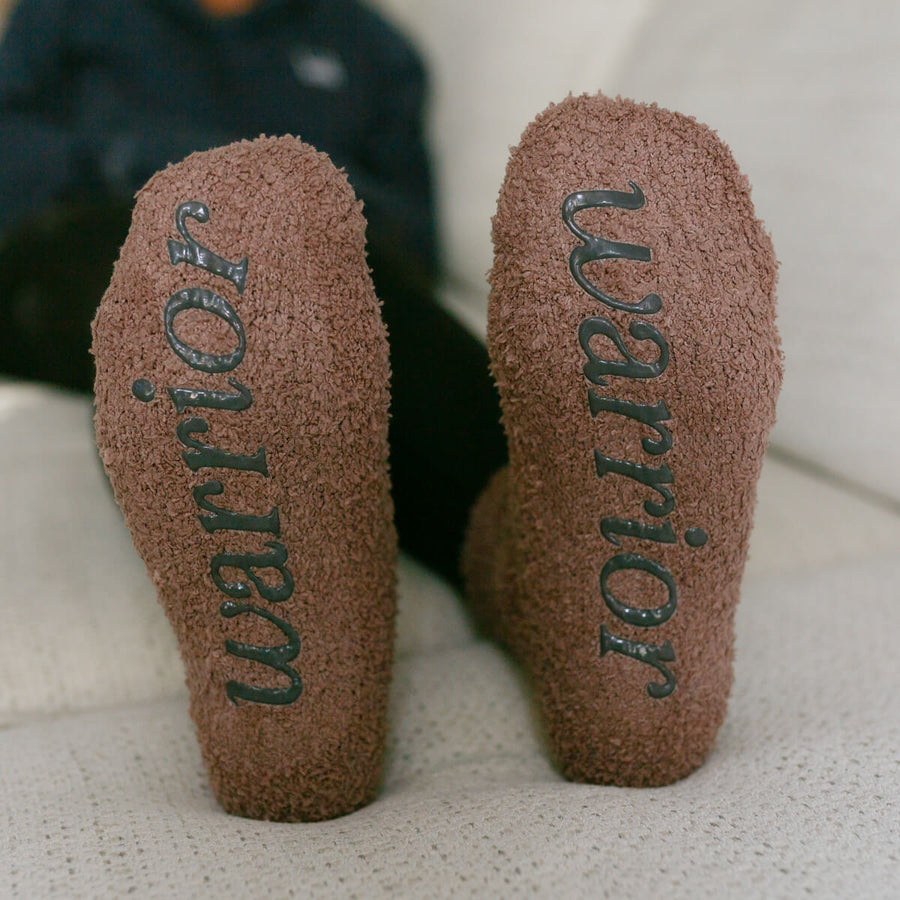 Close-up of tan Rest Day socks showing "wellness" text printed on heel and sole.