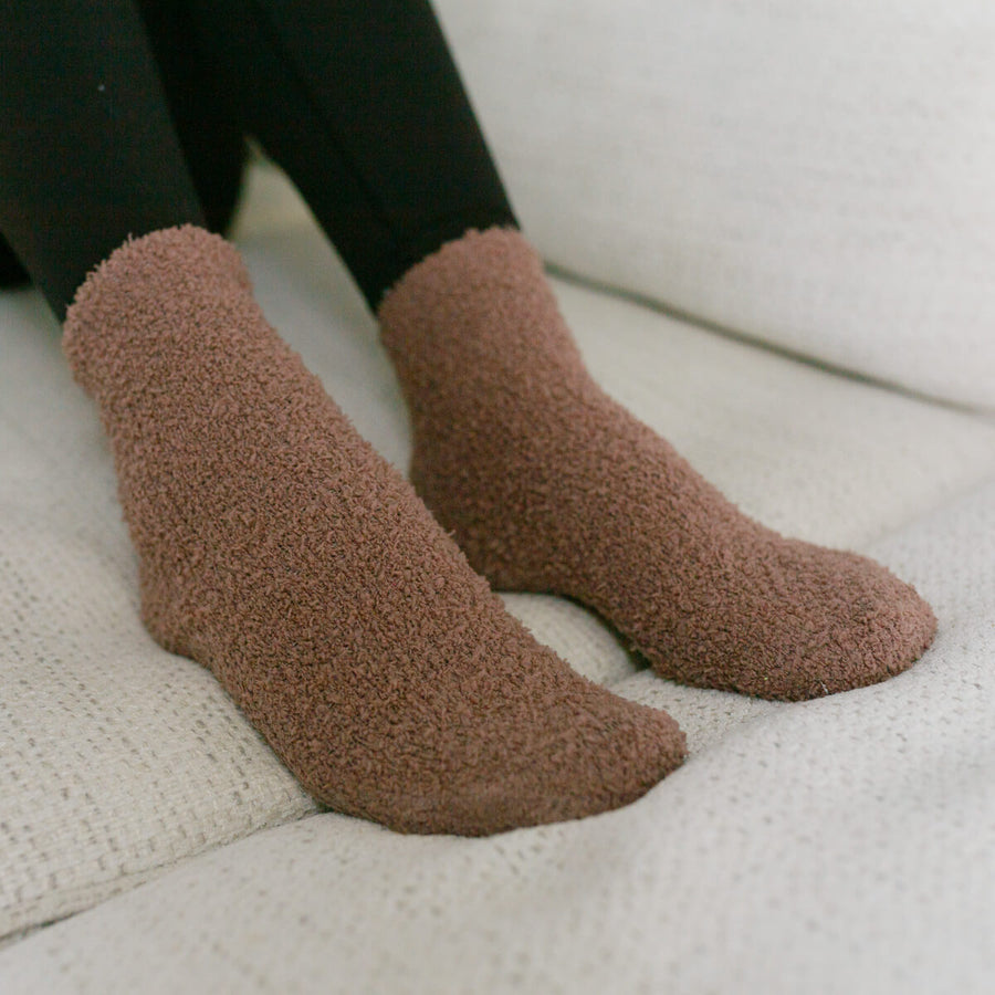 Person wearing taupe fuzzy Rest Day Socks, close-up lifestyle view on couch.