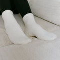 Close-up of white rest day socks displayed on beige cushioned surface.