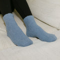 Person wearing blue cozy rest day socks with black pants, seated on cream-colored furniture.