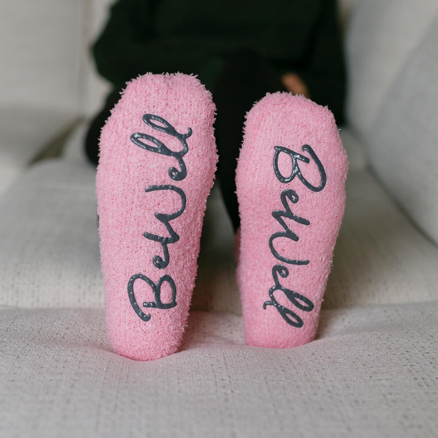 Close-up of pink Rest Day socks with "BeWell" text printed on soles.