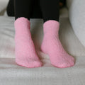 Person wearing pink fuzzy rest day socks with black leggings, seated close-up view.