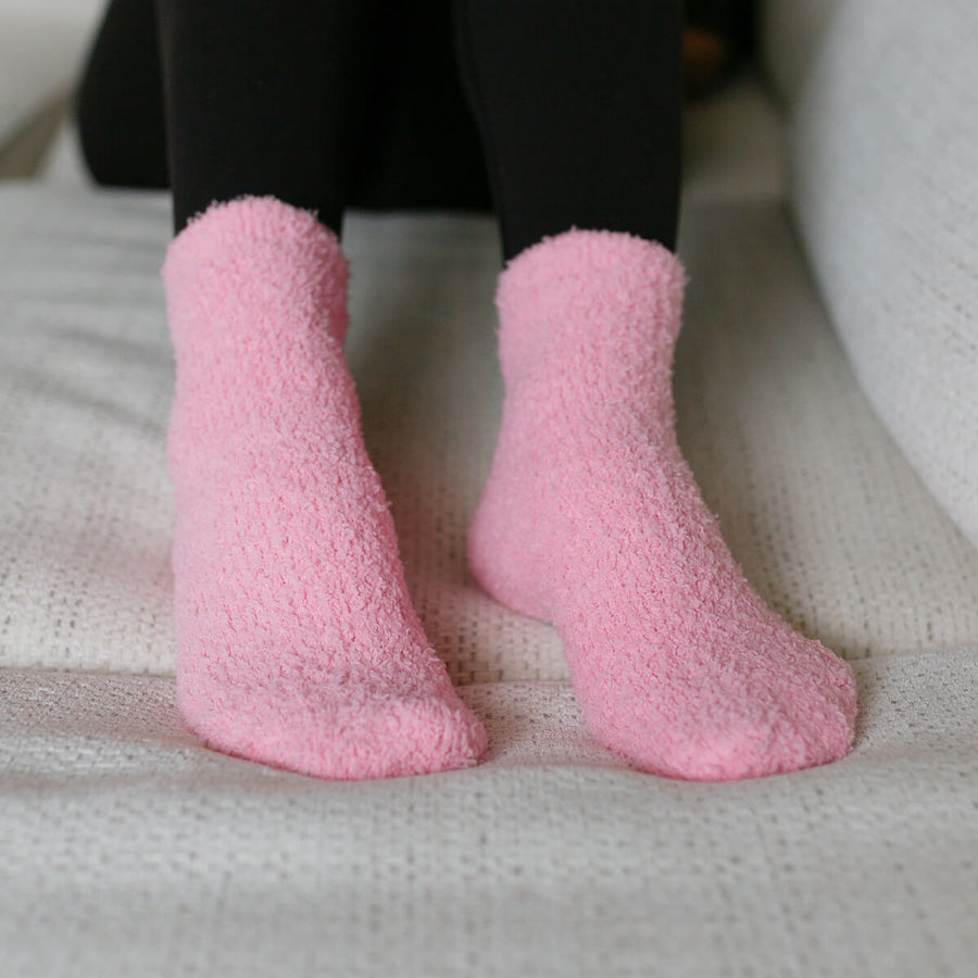 Person wearing pink fuzzy rest day socks with black leggings, seated close-up view.