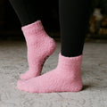 Person wearing pink fuzzy rest day socks with black pants, close-up lifestyle view.