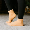 Person wearing peach fuzzy Rest Day Socks with black leggings, close-up side view.