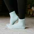 Person wearing black leggings and light blue fuzzy Rest Day socks, close-up detail view.