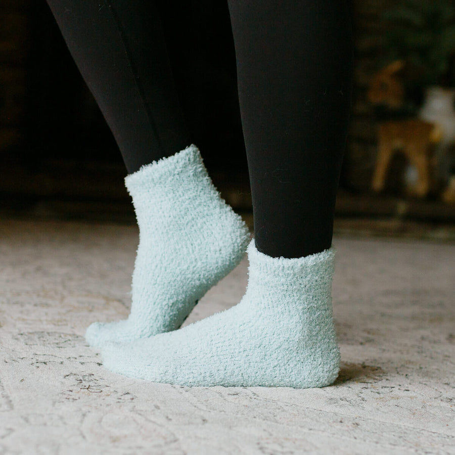 Person wearing black leggings and light blue fuzzy Rest Day socks, close-up detail view.