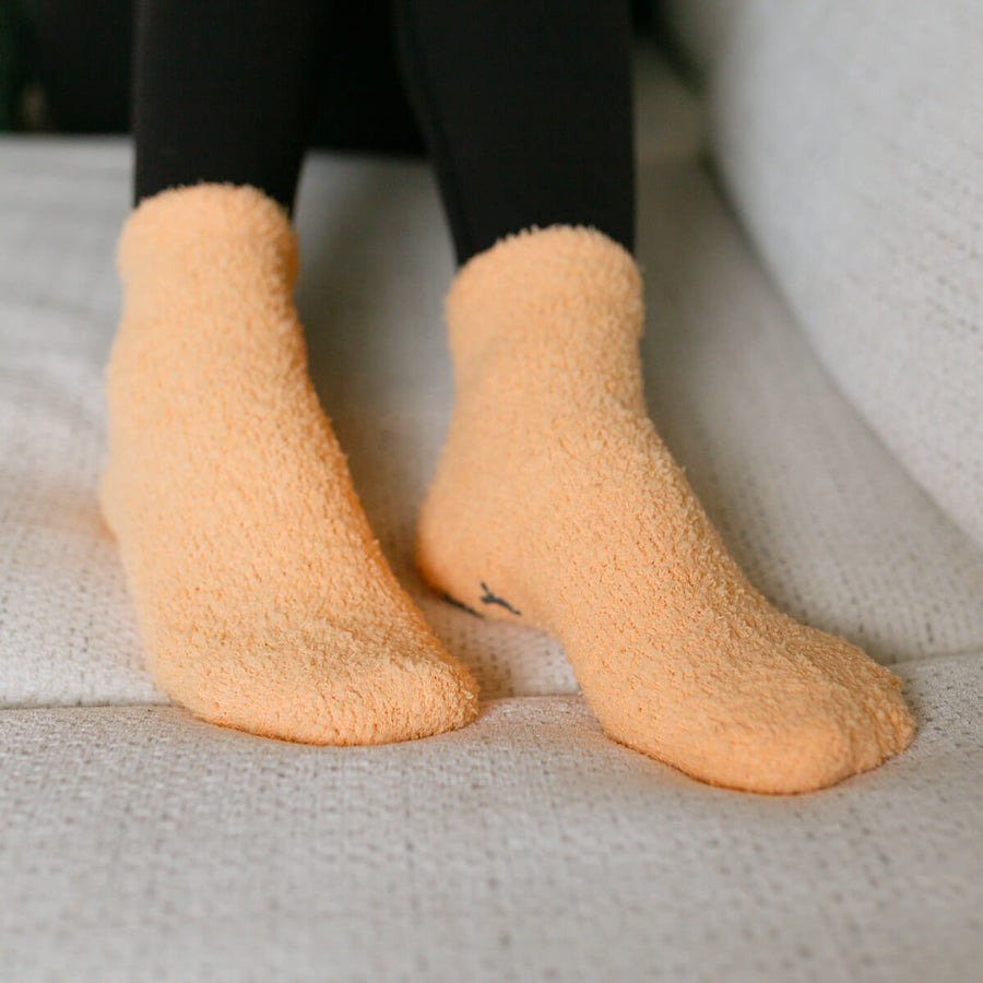 Person wearing peach Rest Day socks, close-up detail view on seated figure.