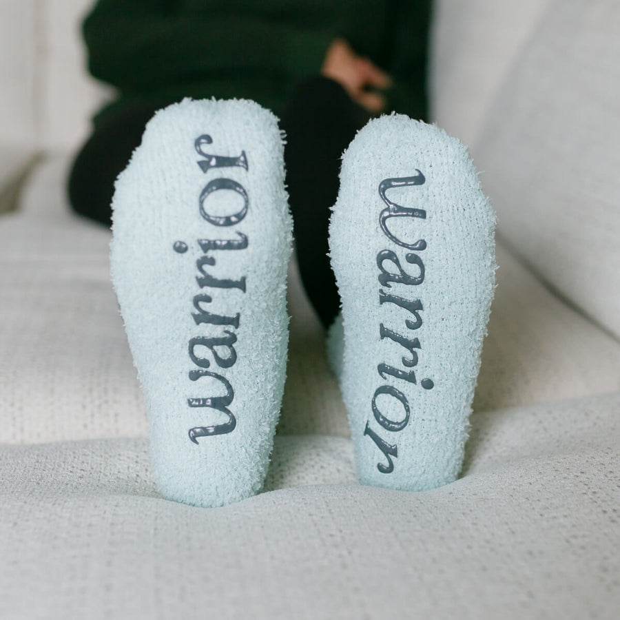 Close-up of light blue Rest Day Socks with "Warrior" and "Warrior" text printed on soles.