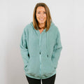 Woman wearing sage green sherpa zip hoodie with front zipper and kangaroo pockets.