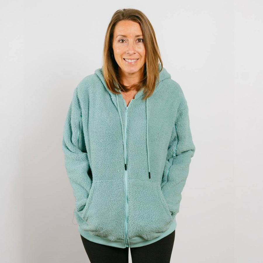 Woman wearing sage green sherpa zip hoodie with front zipper and kangaroo pockets.